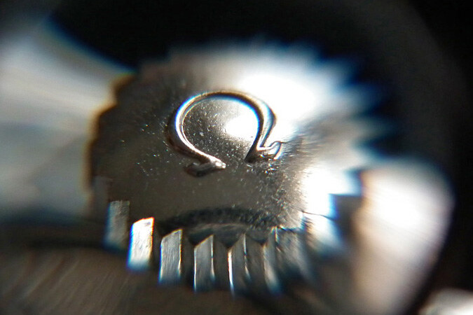 Extreme macro of the Omega crown engraved with the Ω logo, vintage steel case